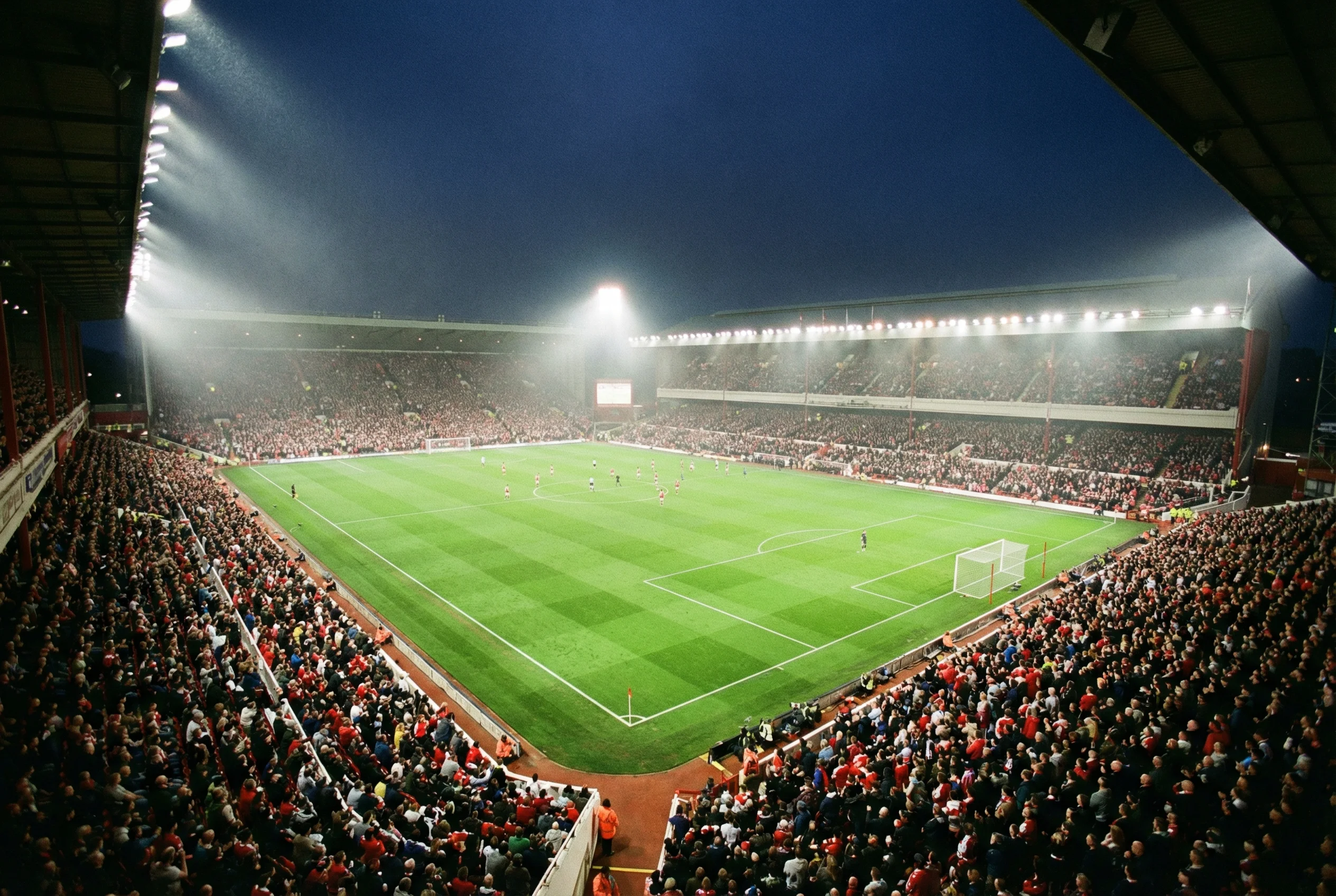 Stadio di Premier League inglese pieno di tifosi durante una partita serale sotto i riflettori